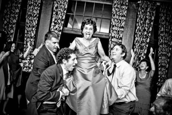 black and white photo -  fun photo of the groom and groomsmen carrying the mother of the groomsman in her chair for the traditional hora dance - photo by New Mexico based wedding photographers Twin Lens